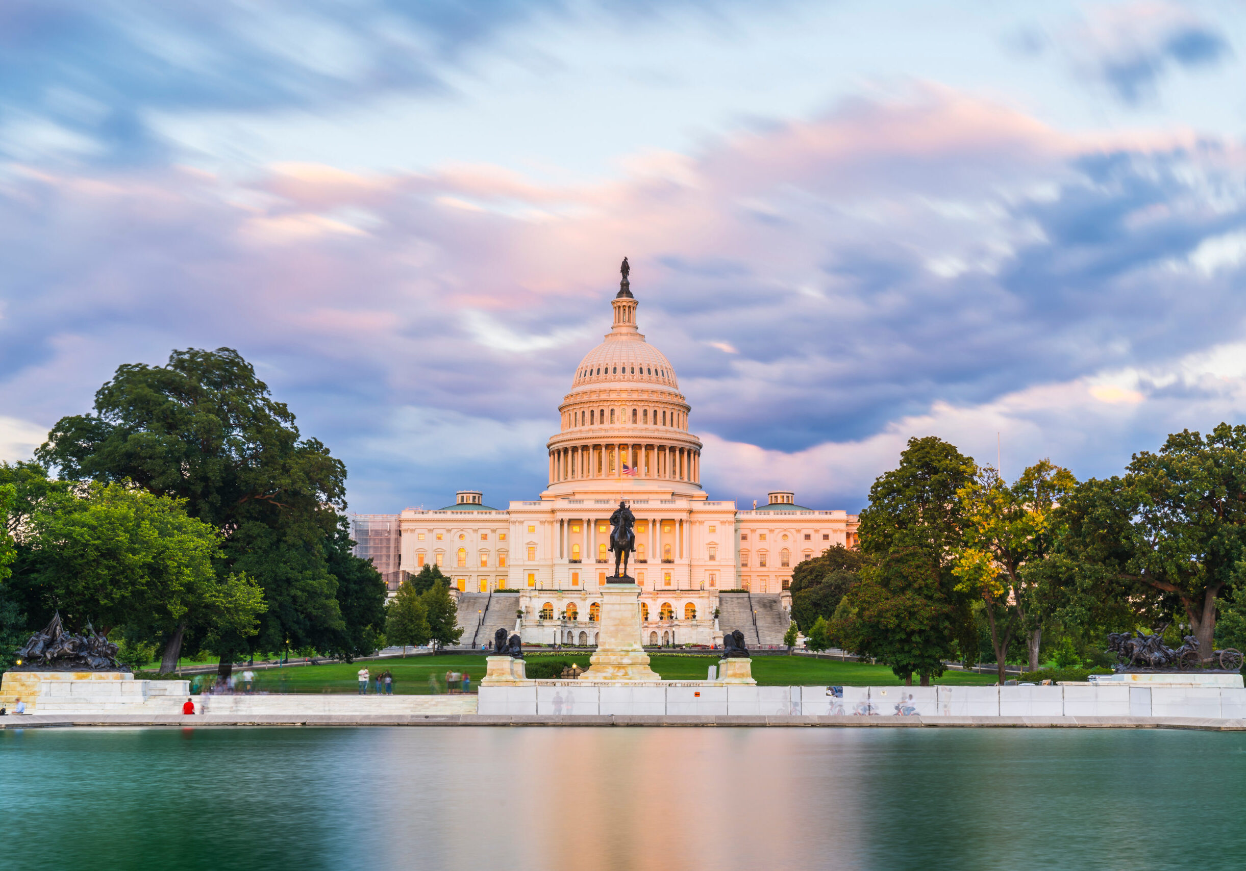 The United States Capitol building at sunset wirh reflection in water.